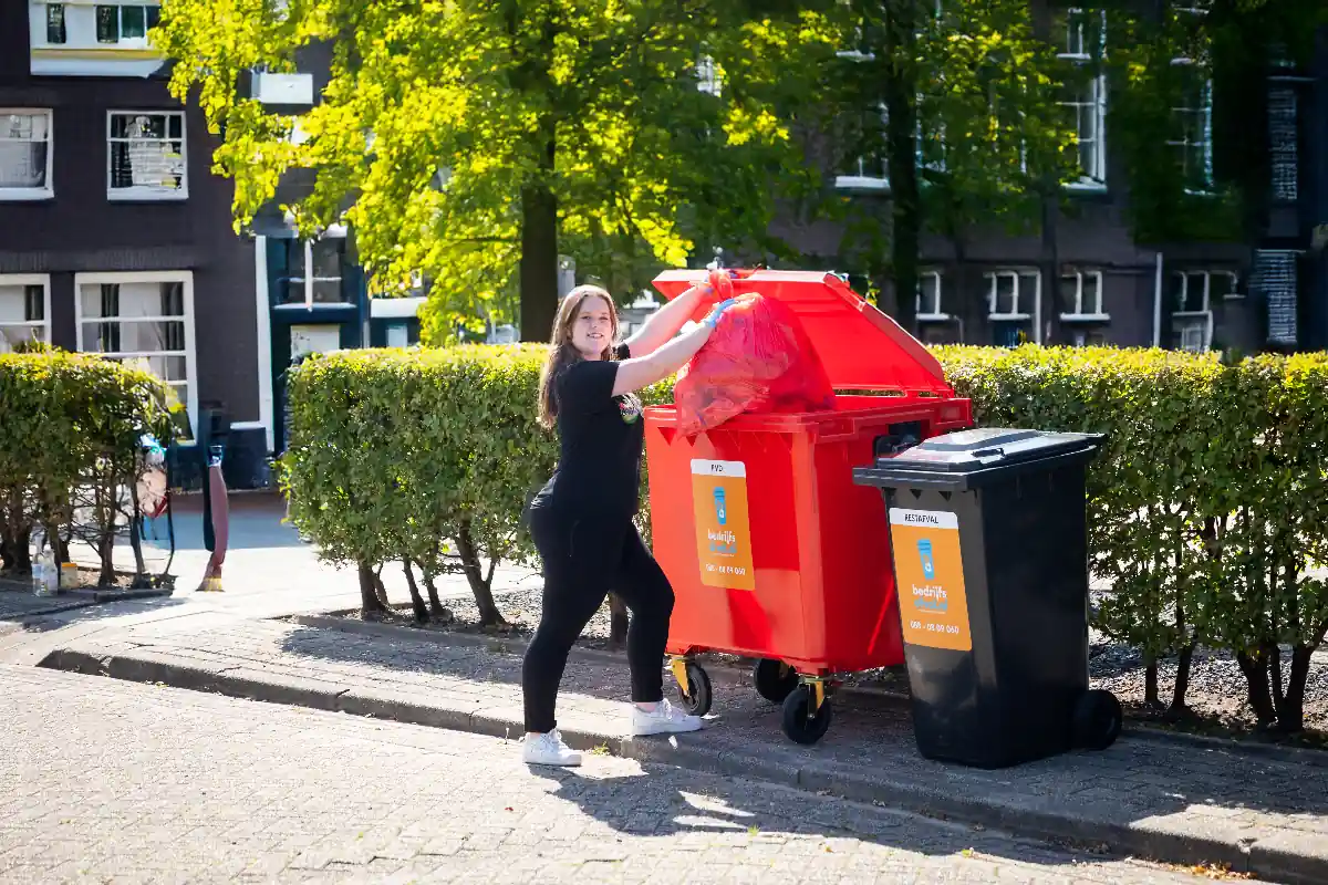 een vrouw die afval weggooit in een rode plastic container die op een straat staat in Amsterdam